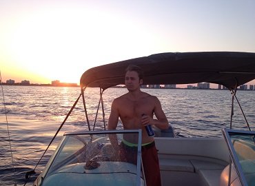 The Book of Rah author Ace Gyllenspetz drinking a beer while driving a boat during a sunset.